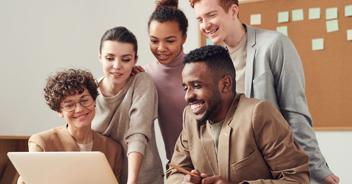 A group of diverse young professionals happily collaborating around a laptop indoors.