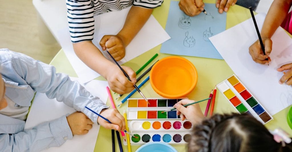 Top view of children painting with watercolors at a preschool art class.