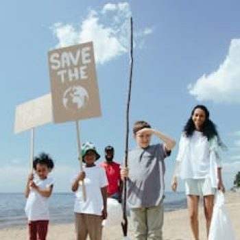 Family and children participating in a beach clean-up, holding save the earth signs.